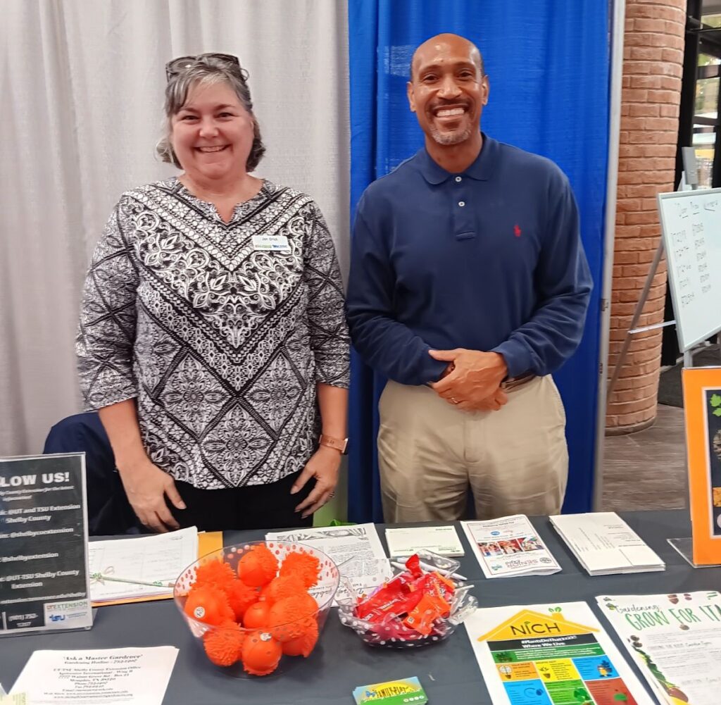 Chris Cooper and a fellow Extension agent standing in a booth at a trade show