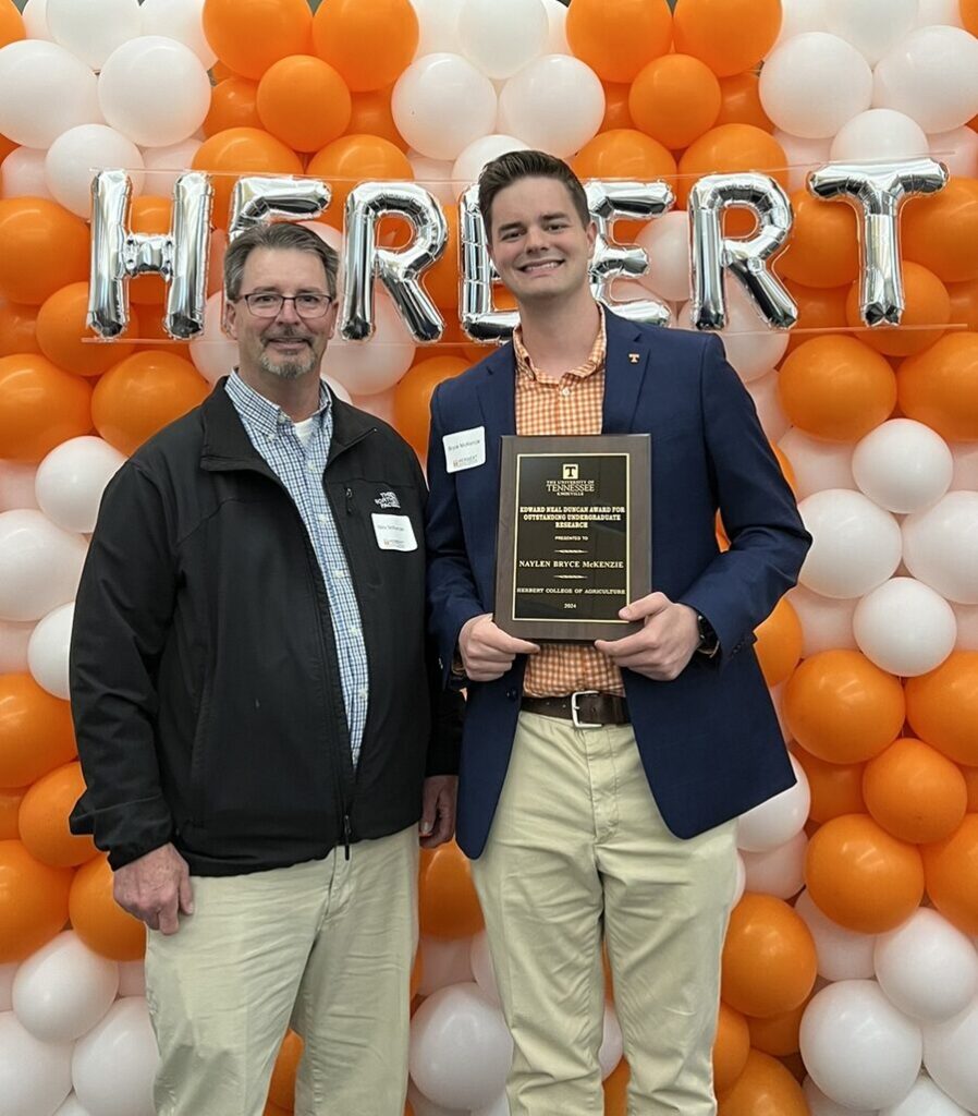 Bryce Mckenzie holding an award in front of a Hebert orange and white balloon wall