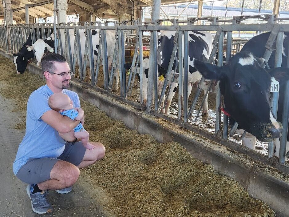 Liz Eckelkamp's husband holding their baby next to dairy cows