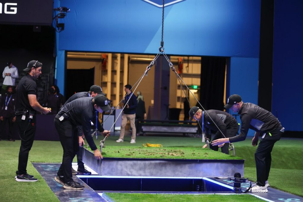 a group of turf experts lowering a plot of turf into the ground