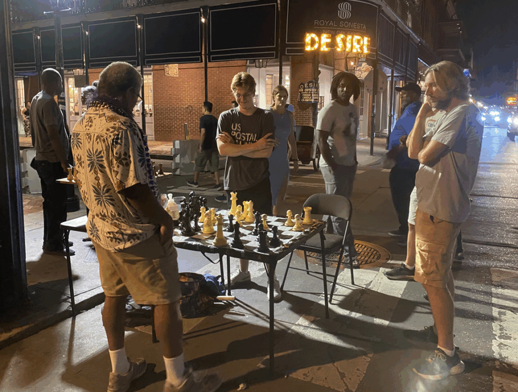 Jacob Friedrich playing chess with a man with a few spectators on a sidewalk
