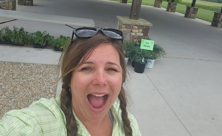 Shalena Durkot taking a selfie with a small number of plants behind her after a successful plant sale.