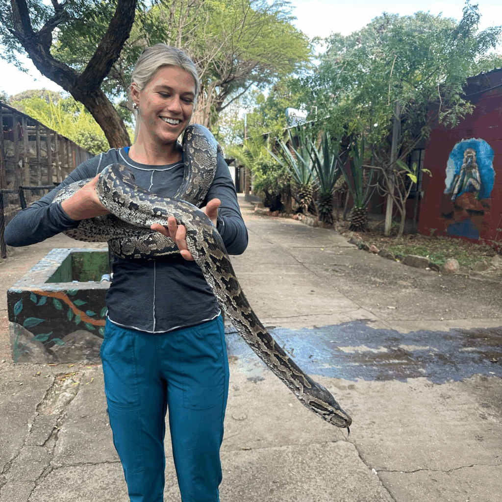 Mason Dunlap holding a ball python in Africa. The snake is wrapped around her shoulders and she smiles.
