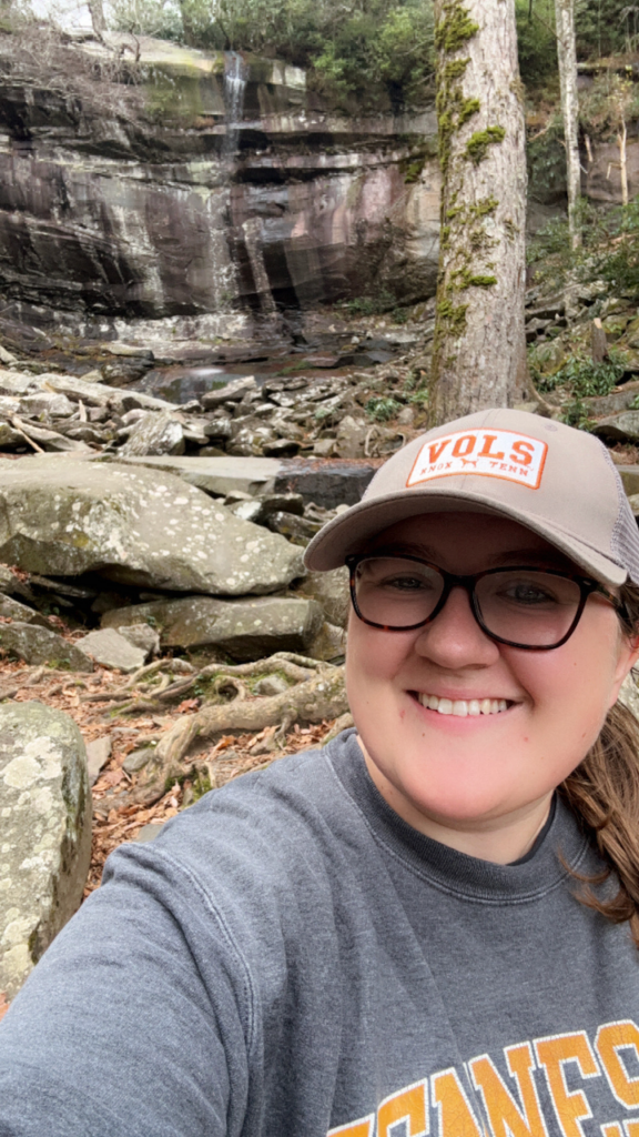 Haley Williamson smiling on a hike while standing in front of a waterfall.