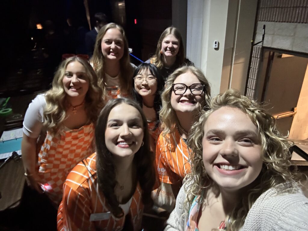 Ally Lay taking a selfie with six students wearing orange clothing.