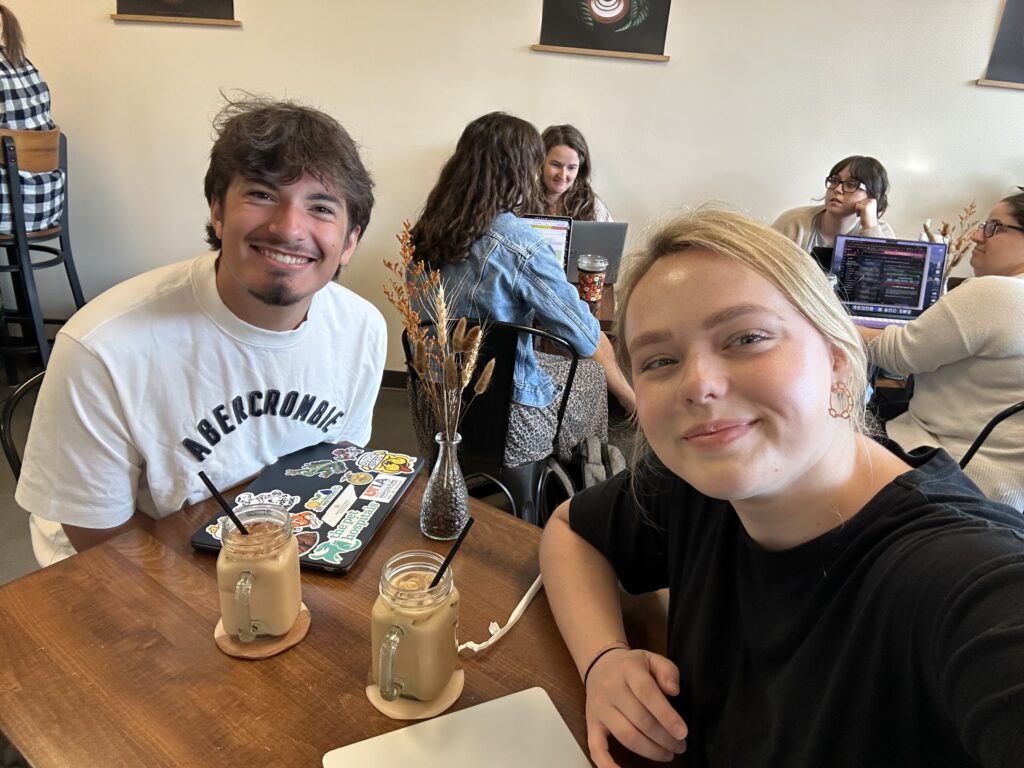 Ally Lay and student are sitting at a wooden table in a café with iced coffees and laptops.