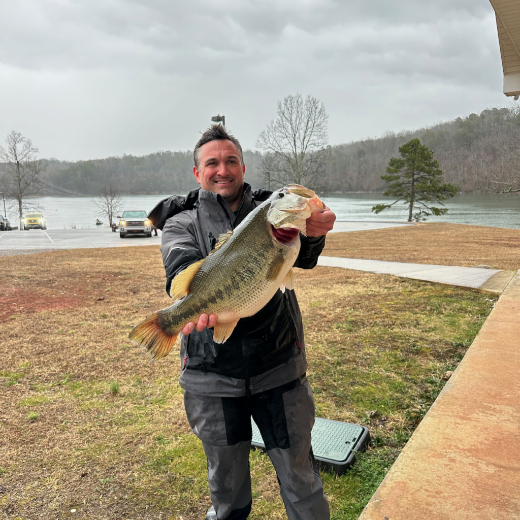 David Bilderback stands outdoors near a lake, holding a large fish.