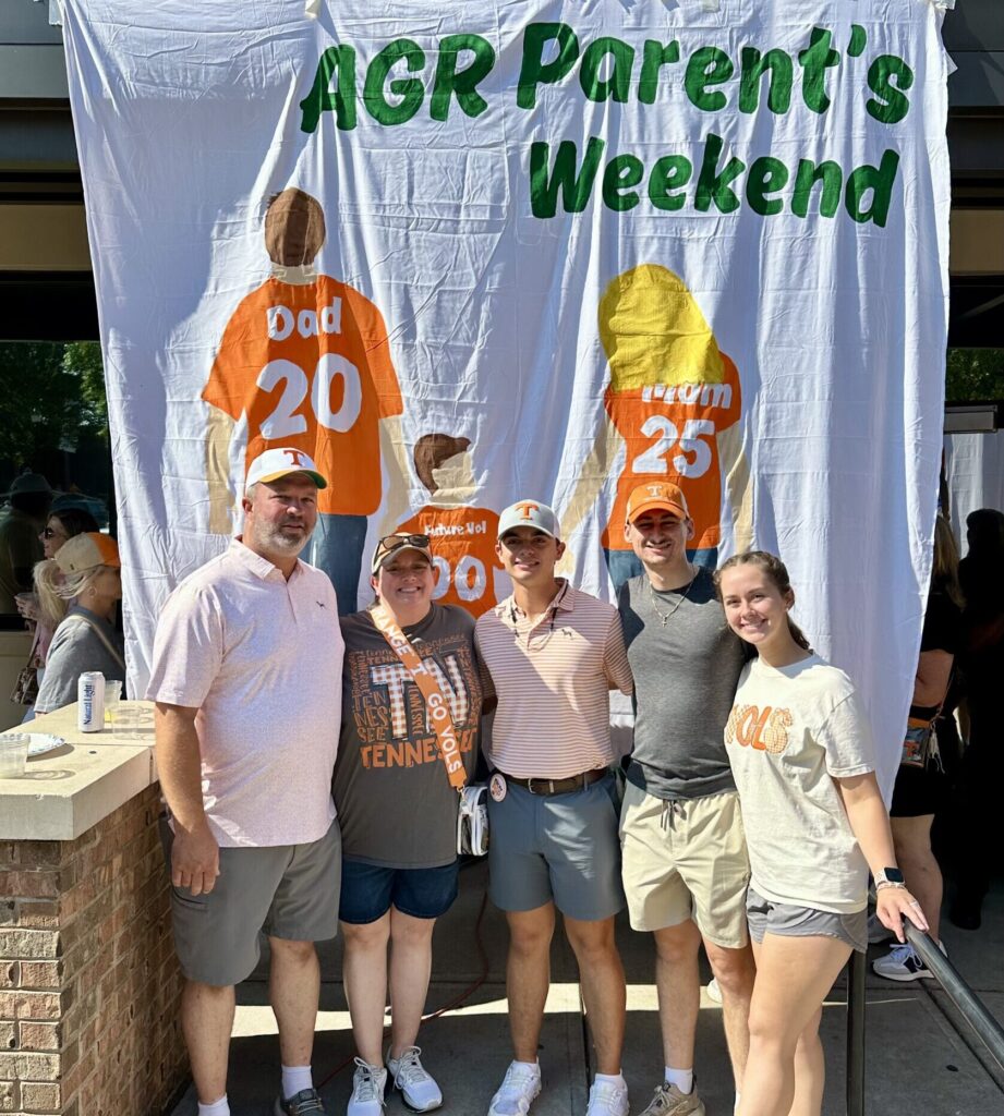 Wyatt Harvey and four others stand in front of a banner that reads "AGR Parent's Weekend."