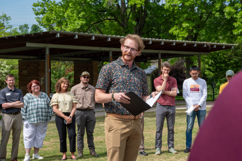 Max Brabson in the UT Gardens, Knoxville, standing in the middle of a circle of people delivering a eulogy