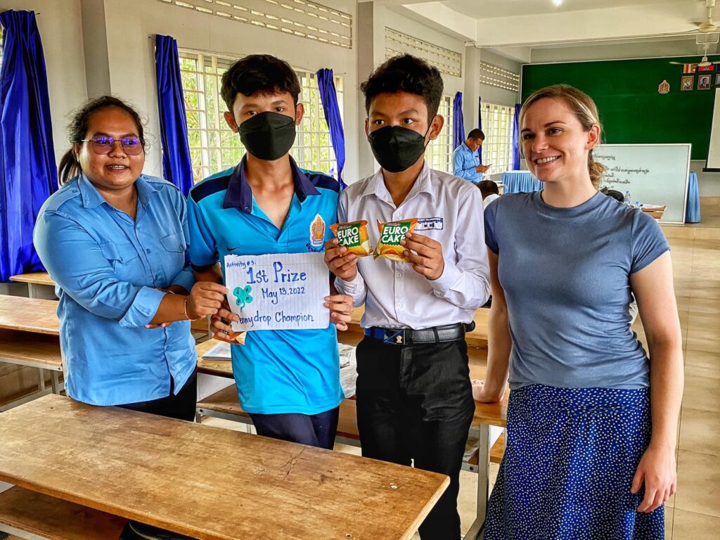 Kristen standing with a fellow teacher and two students holding up a prize for winning first place in a pennydrop competition