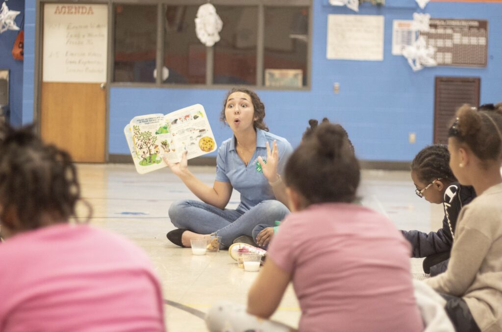 Katie Collins reading a book while sitting in a circle with students