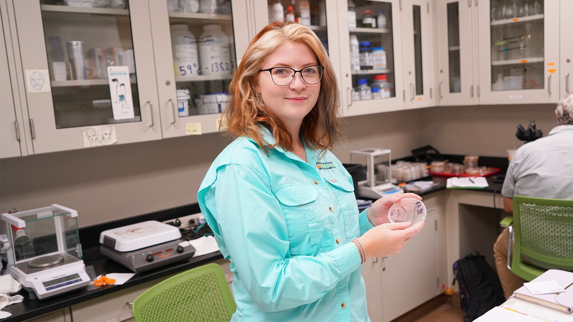 Claire in the lab holding up a Petri Dish