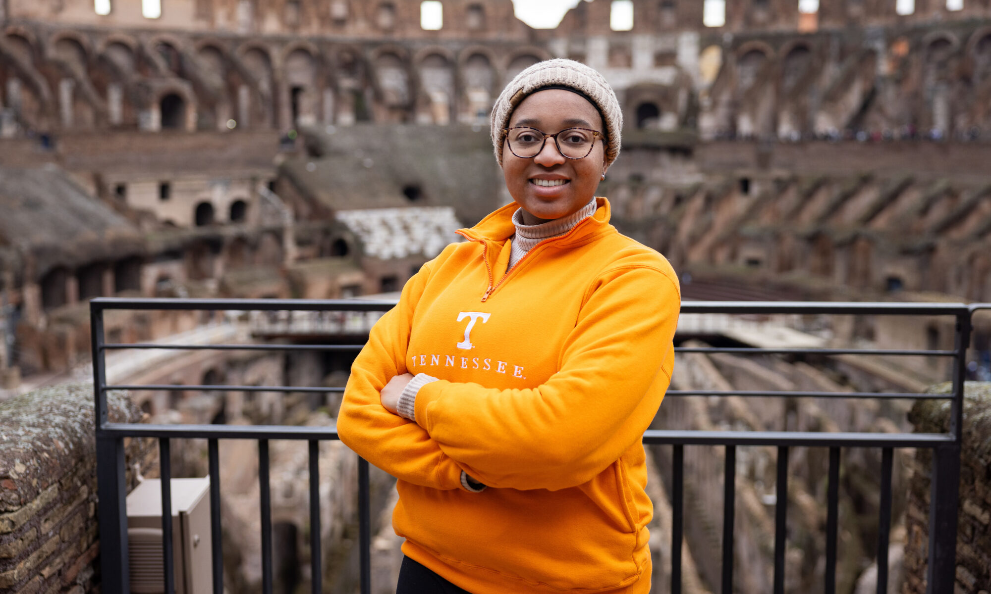 Kyra Barrier wearing a bright orange Tennessee sweater stands inside the Colosseum in Rome, Italy.