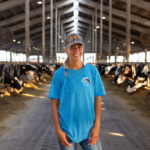 Portrait of Mason Dunlap standing in a barn with rows of dairy cows visible on either side.