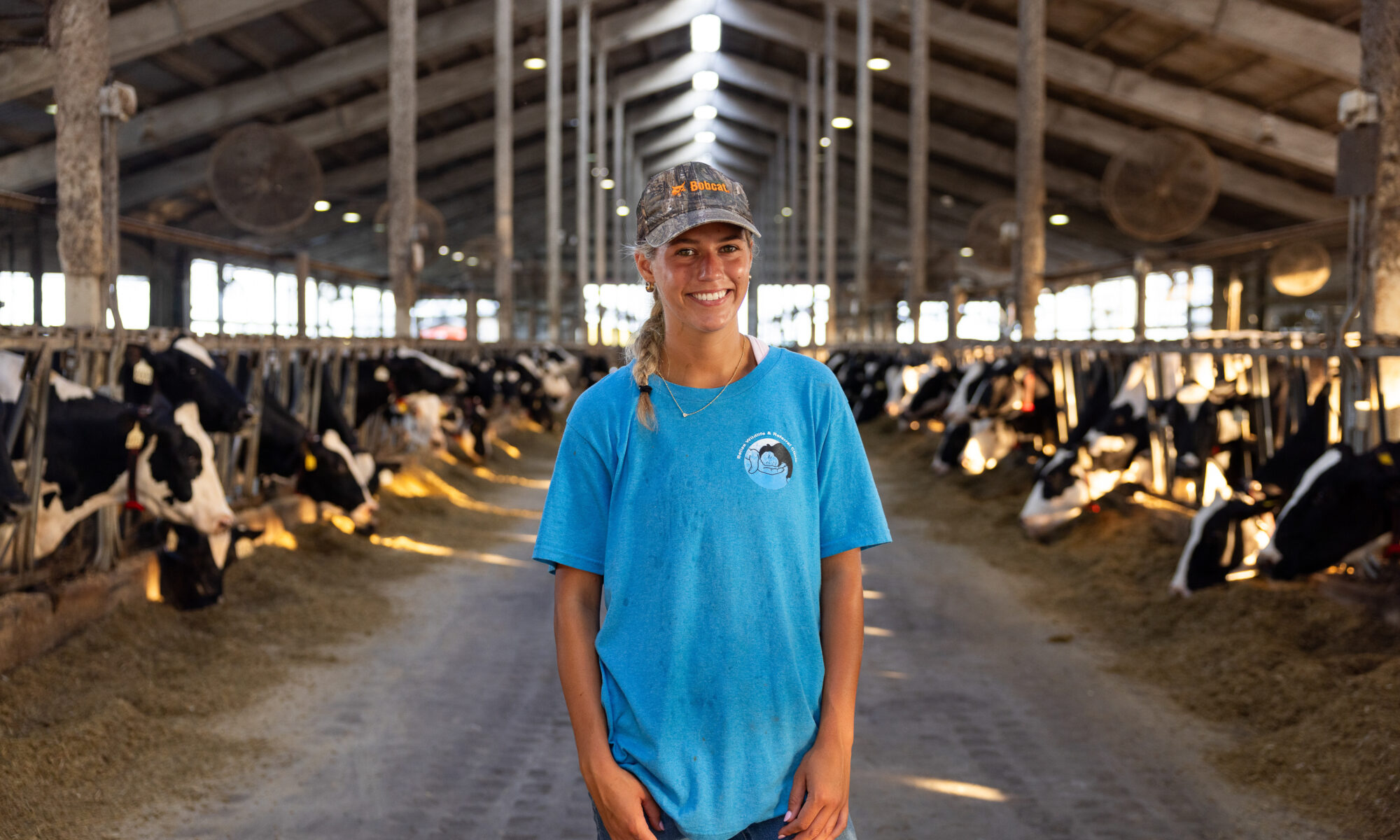 Portrait of Mason Dunlap standing in a barn with rows of dairy cows visible on either side.