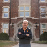 Craig Bacon smiles while wearing a UT Knoxville branded jacket and standing outside Morgan Hall.