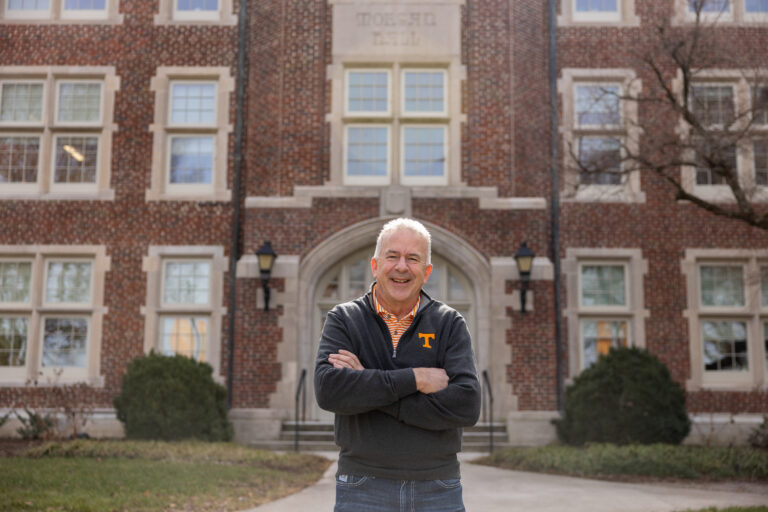 Craig Bacon smiles while wearing a UT Knoxville branded jacket and standing outside Morgan Hall.