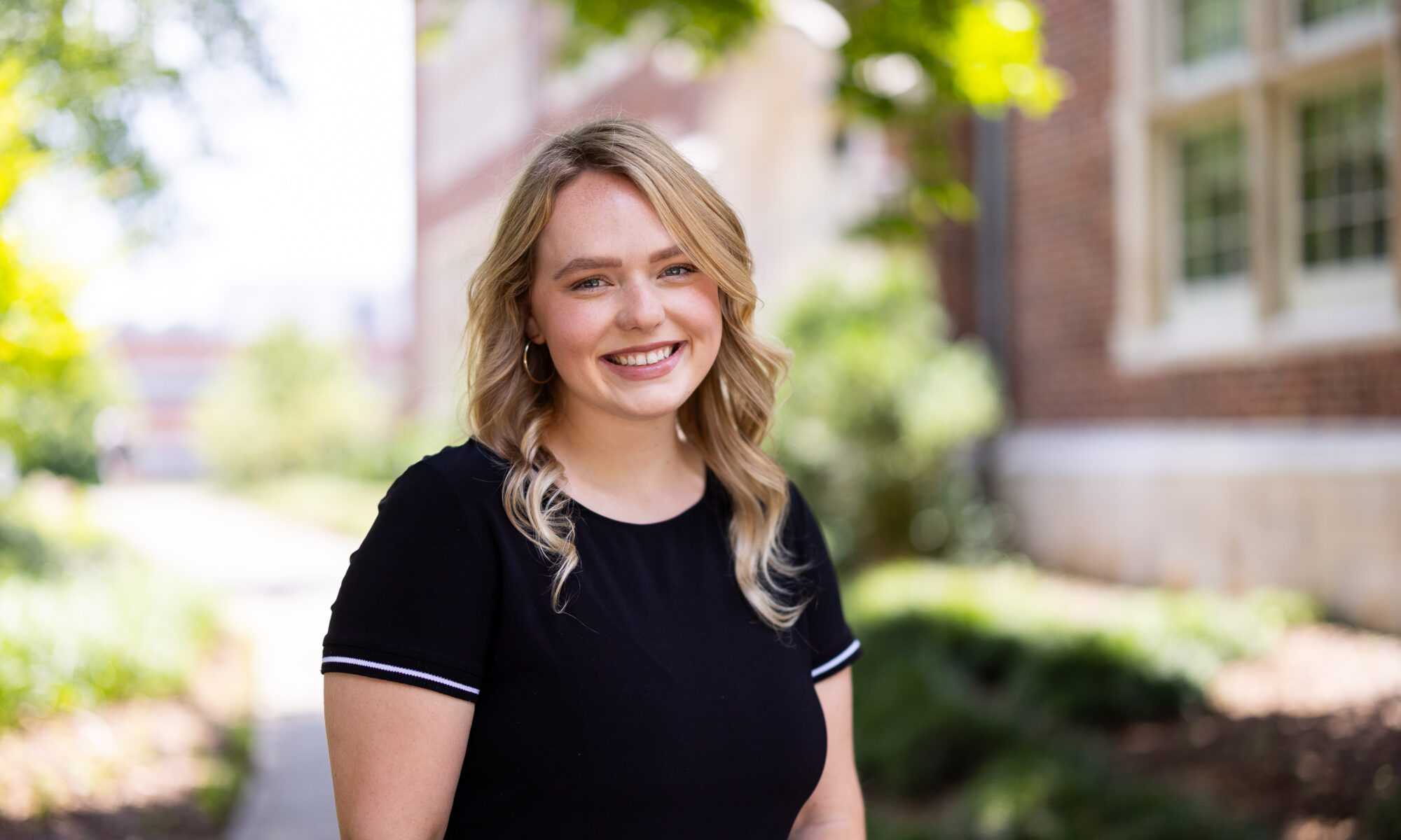 Portrait of Ally Lay standing in front of a brick building.