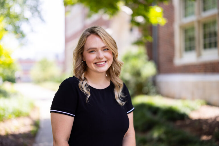 Portrait of Ally Lay standing in front of a brick building.