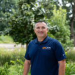 David Bilderback smiles for a photo with trees and greenery in the background.