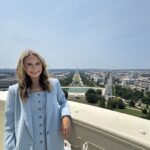 Skylar Baird standing on a balcony overlooking the National Mall in Washington, D.C., with the Washington Monument in the background.