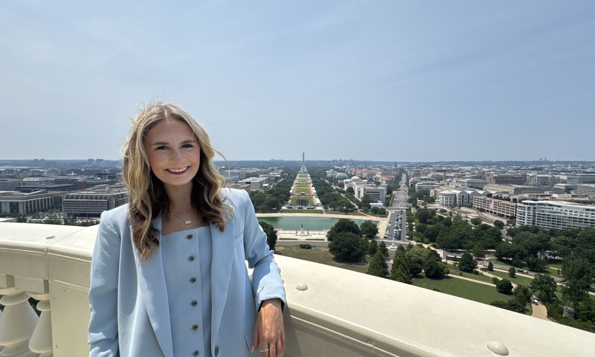 Skylar Baird standing on a balcony overlooking the National Mall in Washington, D.C., with the Washington Monument in the background.