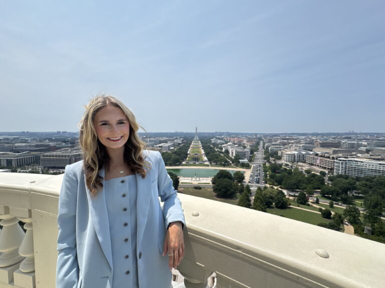 Skylar Baird standing on a balcony overlooking the National Mall in Washington, D.C., with the Washington Monument in the background.