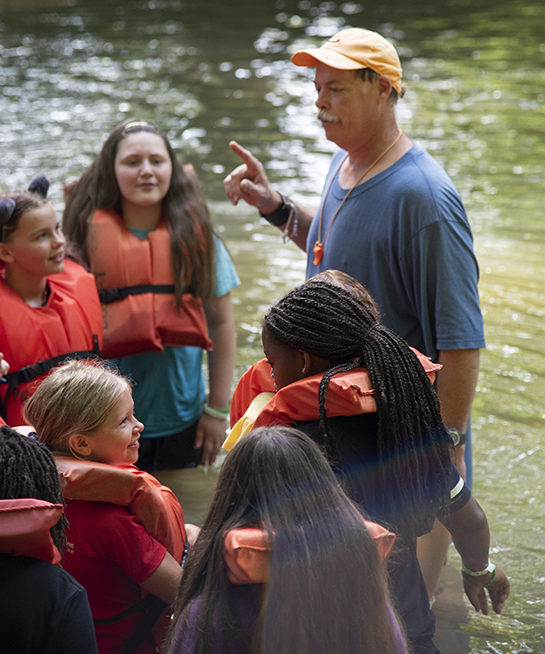 A group of 4-H campers stand in a stream 