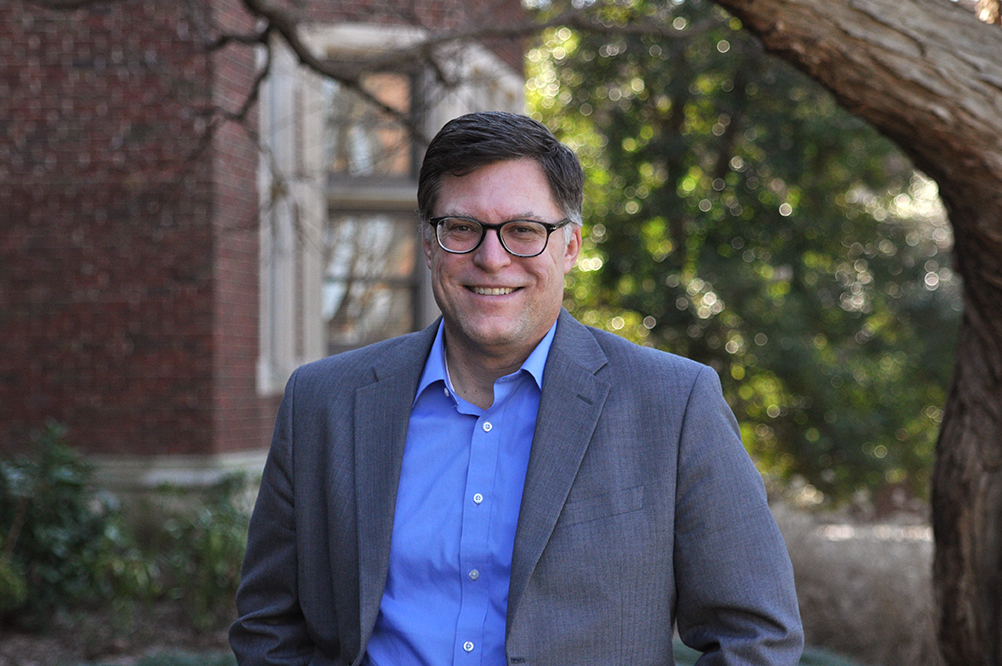 Doug Edlund stands in front of a red brick building with greenery behind him