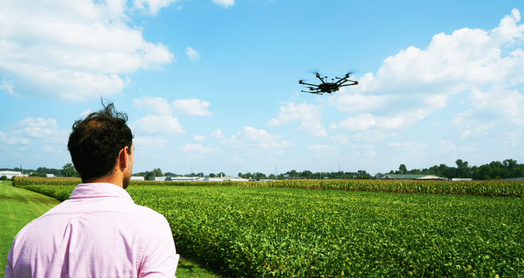 A student controlling a drone over a field of crops