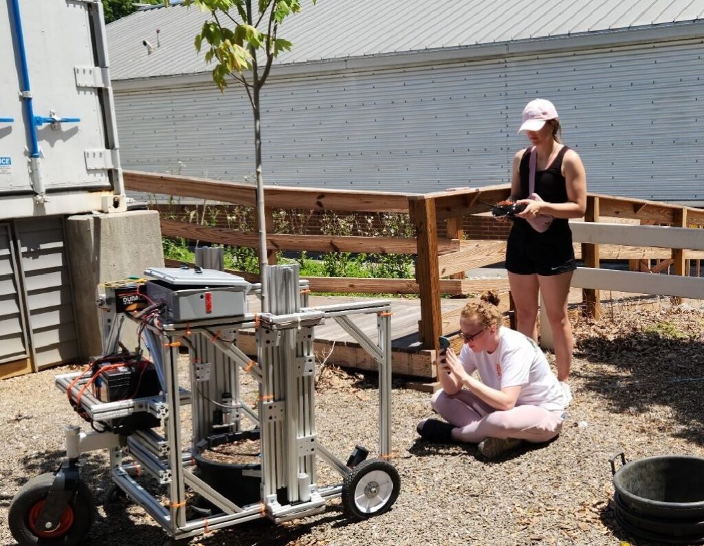 Darlene Player, former BESS Senior Design student, records how an early prototype of the PIPER (Pot-in-Pot Extraction Robot) harvests a red maple in a 15-gallon container with her mobile device at the UT Nursery Research Complex. Fellow Senior Design student, Bailey Millsaps, operates the prototype by remote control.